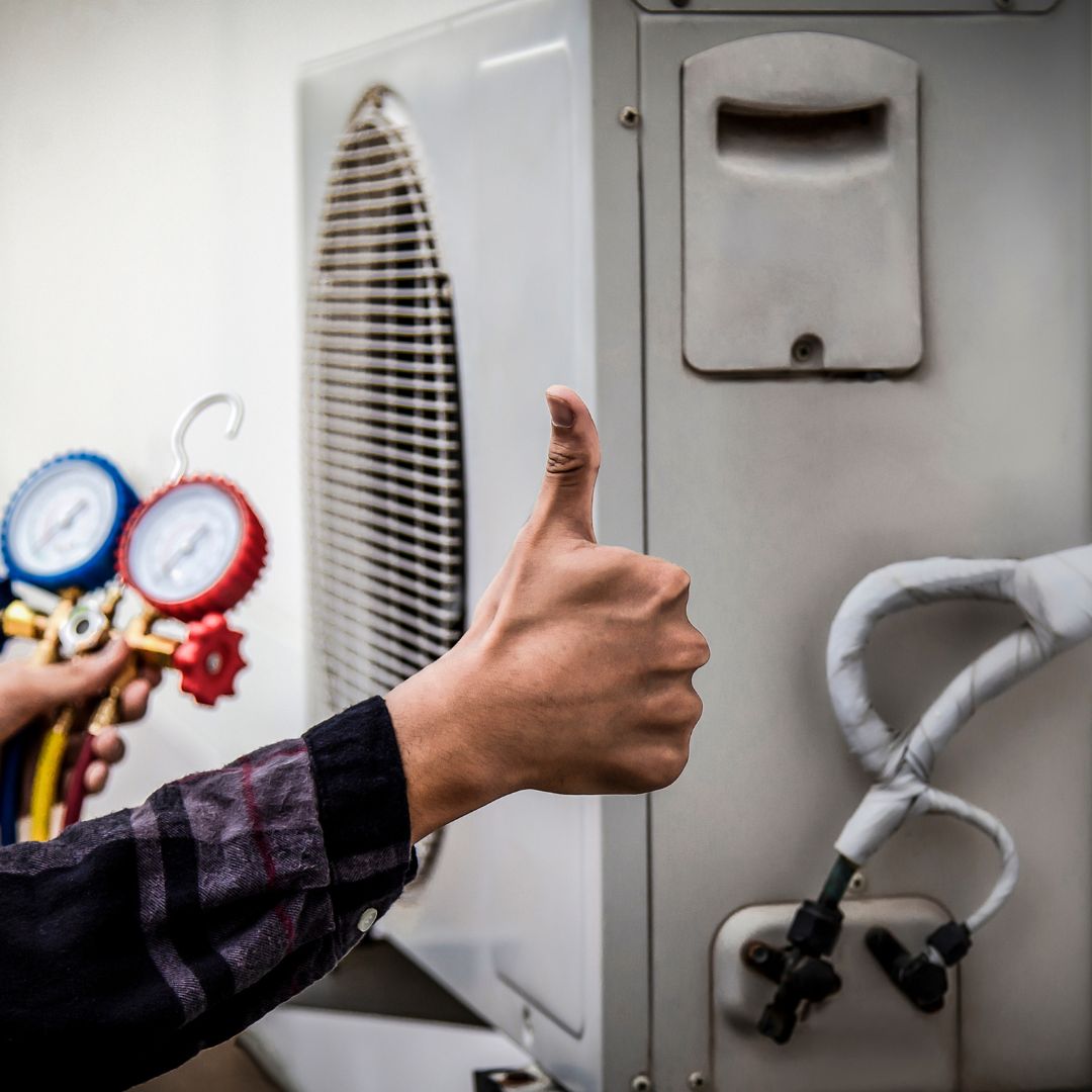Mano sosteniendo un medidor de presión de un sistema de aire acondicionado con un pulgar hacia arriba en señal de aprobación.