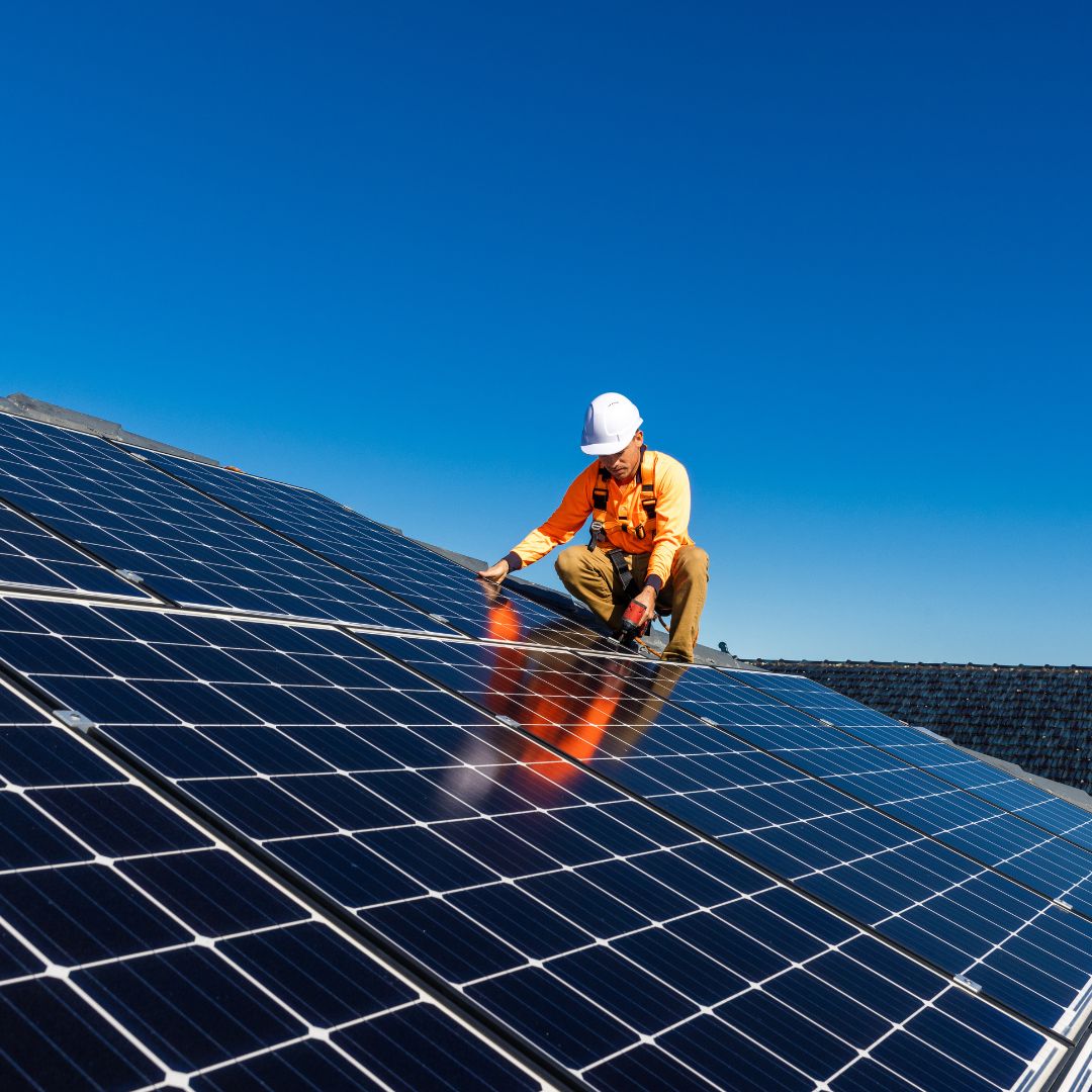 Técnico instalando paneles solares en el techo de una casa bajo un cielo despejado.