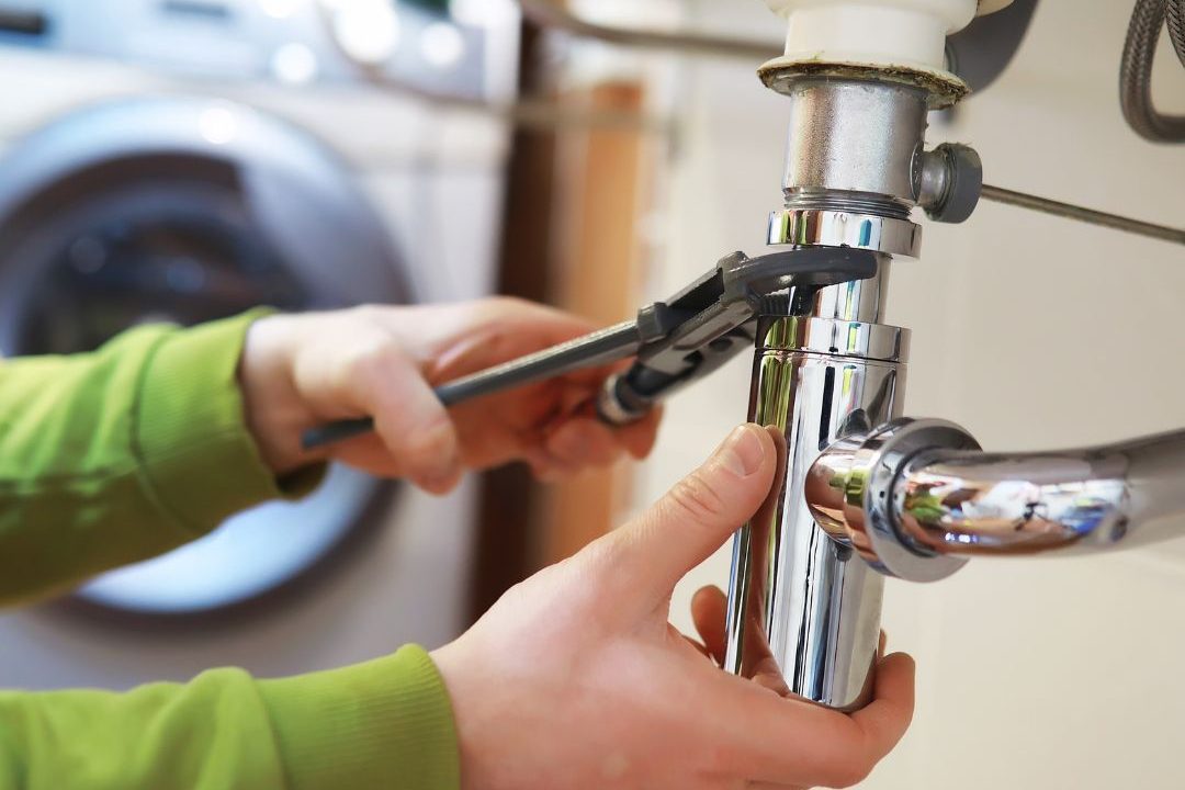 Manos de una persona ajustando una tubería bajo un lavabo con una llave inglesa.